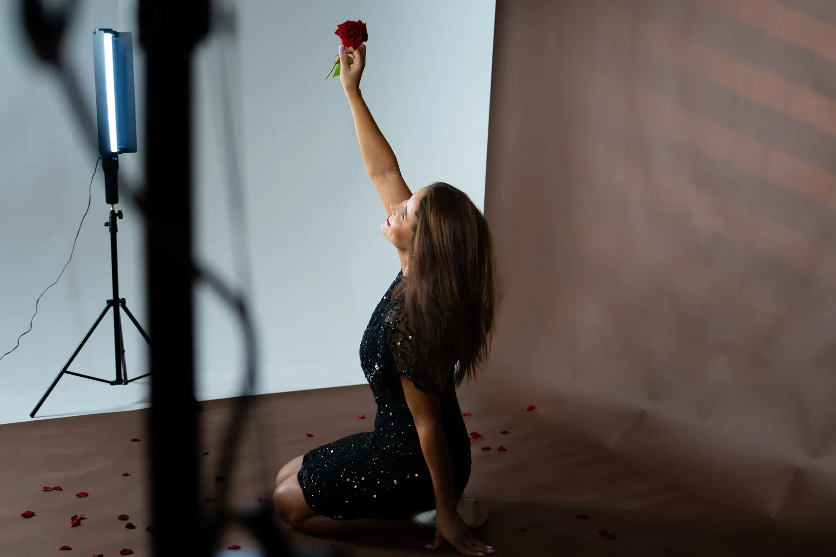 Robe noire à sequins, pose à genoux, une rose levée.