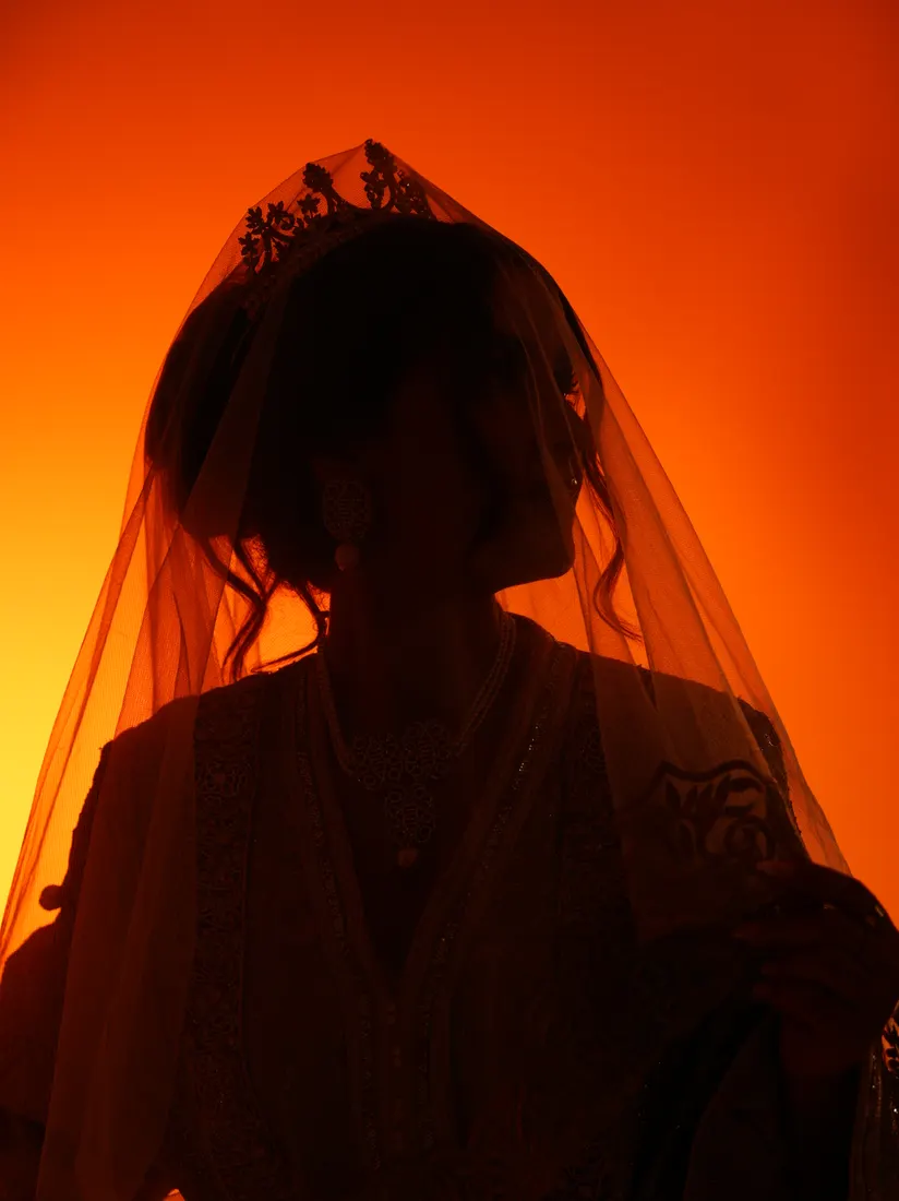 Silhouette voilée de face, en contre-jour sur fond orange.