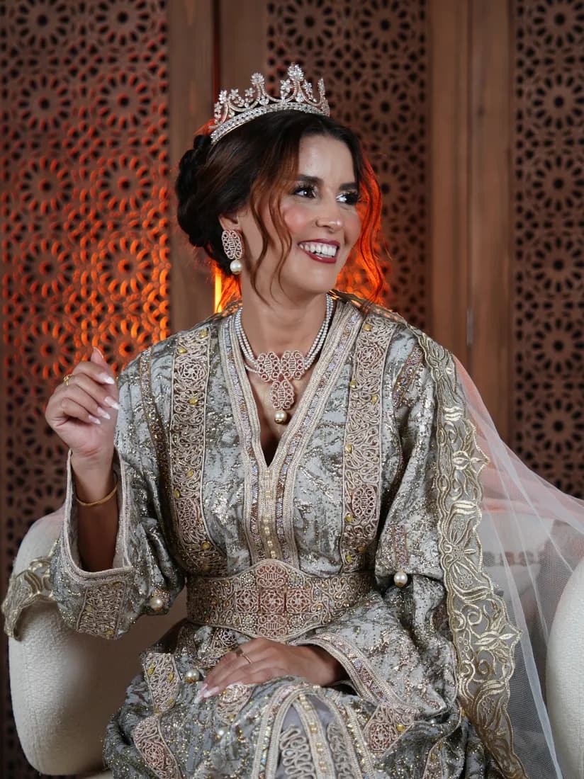 Portrait assis en caftan brodé et couronne, devant un moucharabieh.
