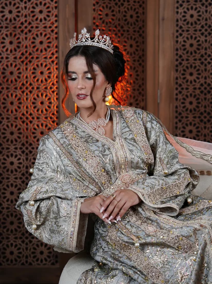 Portrait assis en caftan brodé et couronne, regard baissé.