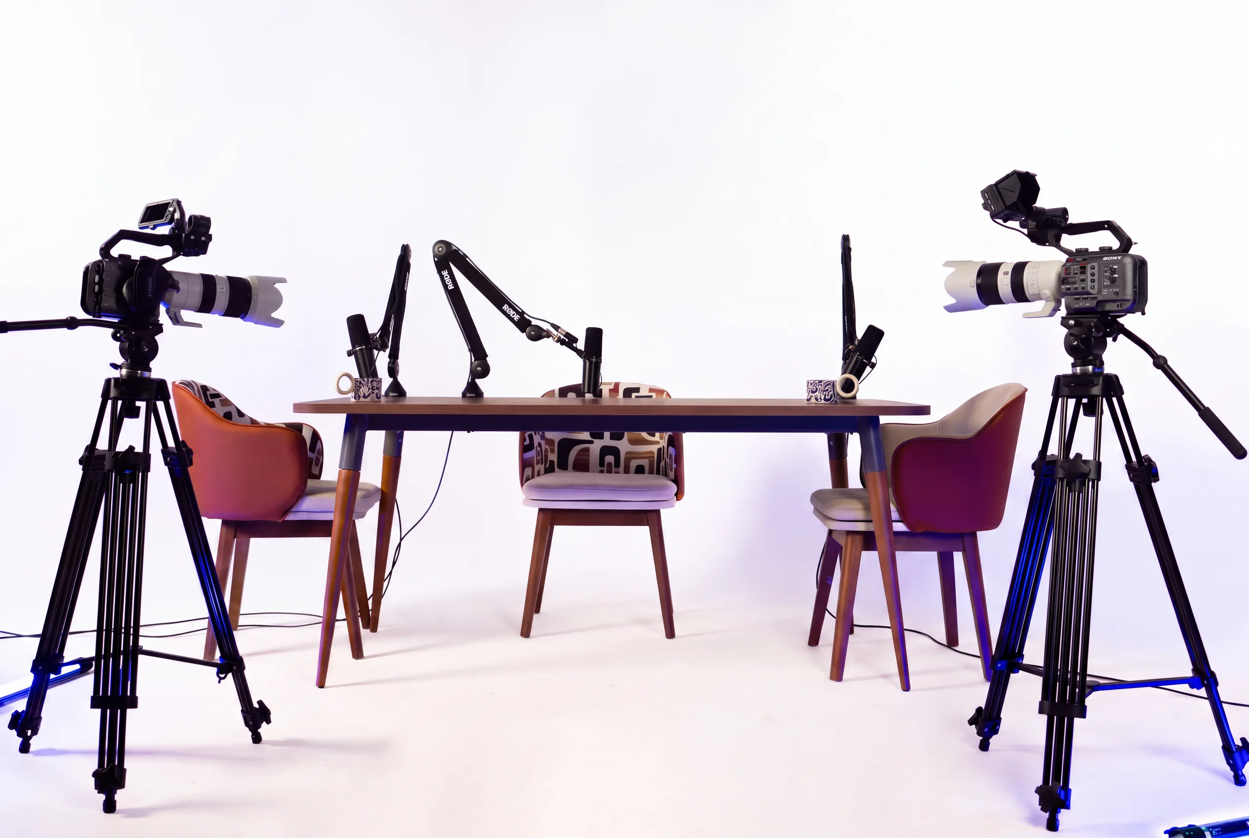 Le plateau ESCAPE ROOM équipé : table en noyer, chaises de couleur et micros sur fond blanc, caméras de part et d'autre.